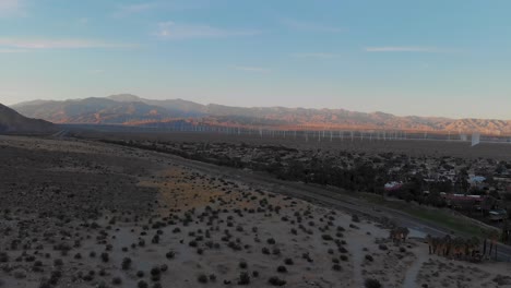 Slow-pull-back-over-desert-brush,-windmills-outside-small-town-drone-shot