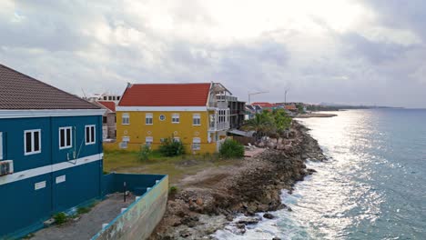 Iconic-blue-and-yellow-houses-along-coast-of-Punda-Pietermaai-Willemstad-Curacao-at-sunrise,-aerial-pan