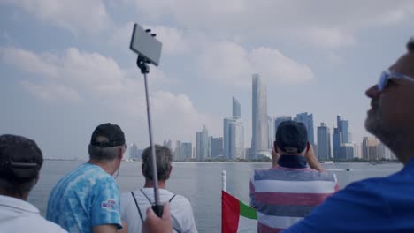 Abu-Dhabi,-Vereinigte-Arabische-Emirate,-Touristen-Machen-Selfies-Und-Bilder-Der-Skyline-Der-Stadt-Von-Einem-Boot-Aus,-Das-Auf-Dem-Meer-Kreuzt