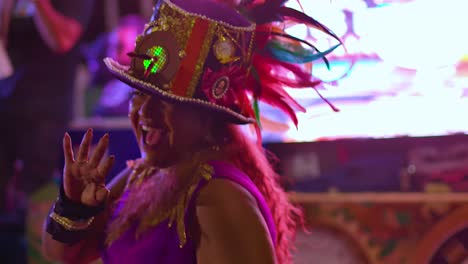 Woman-smiles-blowing-kisses-while-wearing-a-feathery-hat-at-night-during-Carnival