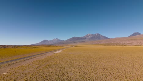 Desert-road-cutting-through-a-vast,-tranquil-Altiplano-landscape-in-Chile,-under-a-clear-blue-sky
