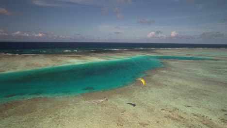 A-single-kite-surfer-gliding-over-clear-turquoise-waters-near-a-cay-during-daytime,-vibrant-and-serene,-aerial-view