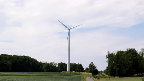 A-wind-turbine-is-tall-and-white,-standing-in-a-field