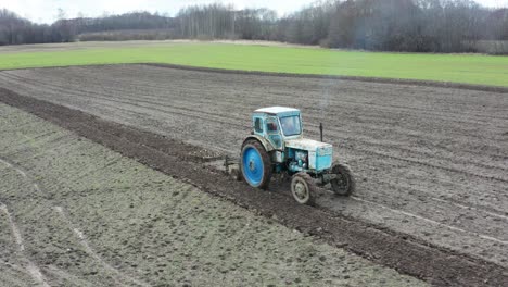 Farmer-drive-old-rusty-tractor-on-farmland,-emit-blue-exhaust-gas-in-air