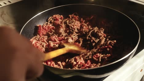 Person-cooking-ground-meat-in-a-pan-on-a-stove,-stirring-it-with-a-spatula