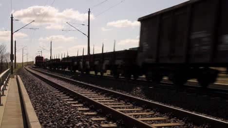 Freight-train-speeding-on-tracks-under-sunny-sky,-blurred-motion,-daytime