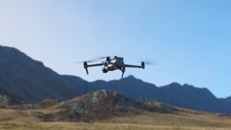Drone-descends-to-land-on-grassy-field-with-mountains-in-background
