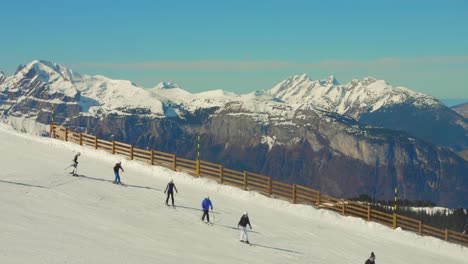 People-skiing-on-snowy-slope-with-wooden-fence-above-mountain-valley