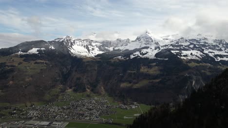An-aerial-view-of-Glarus,-Switzerland's-smallest-canton-capital,-nestled-amidst-mountains-at-the-base-of-the-Glärnisch-ridge,-surrounded-by-snow-capped-peaks,-exuding-the-allure-of-the-Swiss-Alps