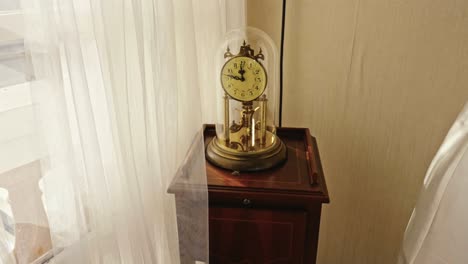 antique-table-clock-inside-a-glass-dome-on-a-table-in-a-room-with-lots-of-natural-light
