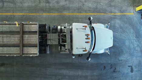 Drone-top-down-rising-ascend-above-semi-truck-and-empty-trailer-in-warehouse