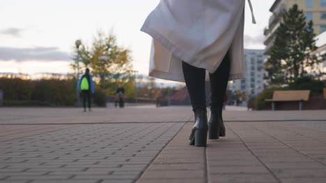 Low-angle-view-of-woman-walk-on-city-sidewalk-and-coat-flutter-in-wind