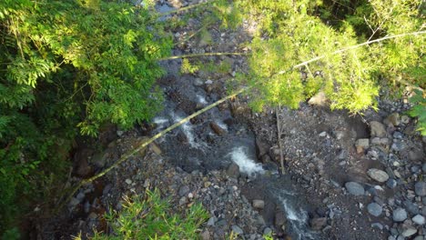 Drone-shot-descending-vertically-down-onto-a-small-stream-of-natural-fresh-water-flowing-down-a-mountain-surrounded-by-trees-in-Risaralda,-Colombia