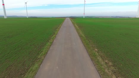 Narrow-Road-Through-Wind-Turbines-In-Green-Fields