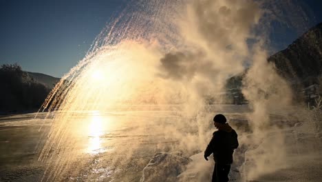 Person-throwing-boiling-water-in-air,-turning-into-snow-in-front-of-winter-sunset,-Slow-motion-Handheld