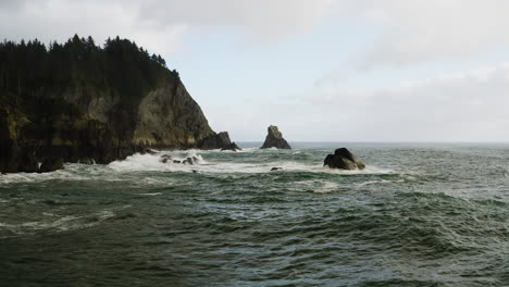 Low-flight-over-rough-Pacific-Ocean-surf-on-Oregon-Coast,-towards-small-sea-stack