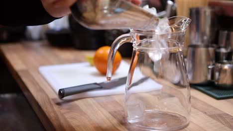 Barista-preparing-a-pitcher-of-lemonade-by-pouring-ice-into-a-pitcher-at-a-restaurant-bar
