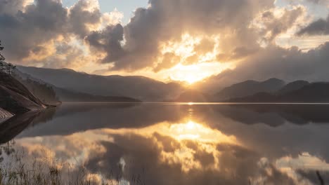The-setting-sun-shines-through-the-heavy-clouds-above-the-calm-lake-in-the-nordic-landscape