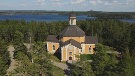 Laukaa-Church,-Finland,-dolly-out-drone-shot-of-the-old-wooden-church-amidst-lakes-and-forest-on-a-beautiful-summer-day