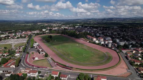 Drohnenaufnahme-Rund-Um-Die-Rennbahn-Und-Die-Rugbyfelder-Der-Stadt-Feurs-Mit-Der-Stadt-Im-Hintergrund,-Département-Loire,-Frankreich