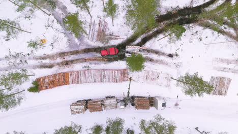 Forwarder-and-grapple-loader-move-and-load-logs-in-snowy-woodland,-top-drone