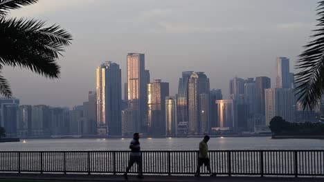 Residentes-Disfrutando-De-Un-Paseo-Matutino-Por-La-Corniche-De-Sharjah-Con-La-Vista-Del-Horizonte-De-Sharjah-Al-Fondo.