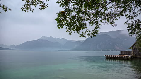 Lake-view-with-mist-unfold-over-majestic-mountains,-nature-timelapse-under-tree-branch