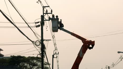 Subiendo-Por-El-Poste-Eléctrico,-Dos-Electricistas-Expertos-Están-Solucionando-Algunos-Problemas-Con-Los-Cables-Eléctricos-En-Un-Barrio-De-Bangkok,-Tailandia.