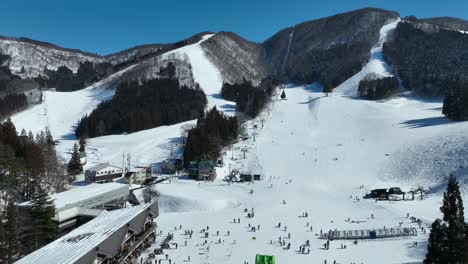 Static-medium-shot-of-bottom-of-ski-run,-skiers-arriving-at-base-of-mountain-lining-up-for-the-chairlifts