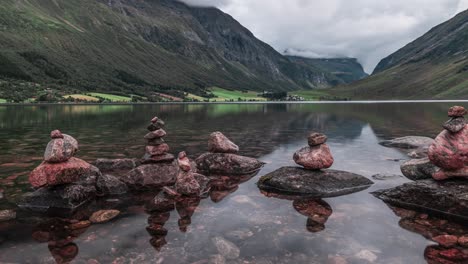 Peculiar-stone-cairns-stand-on-the-edge-of-the-shallow-lake,-surrounded-by-mountains-covered-in-forest