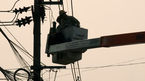 Electric-repairmen-hoisted-on-a-crane-to-reach-the-affected-parts-of-an-electric-wire-and-post-at-a-neighborhood-in-Bangkok,-Thailand