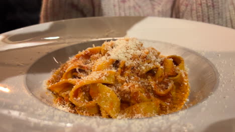 A-waiter-grating-parmesan-cheese-on-bolognese-tagliatelle-pasta-at-a-restaurant,-traditional-Italian-food,-4K-shot