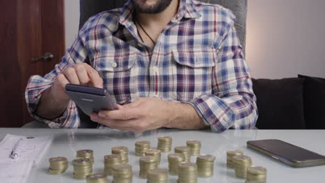 Close-up-of-man's-hands-doing-accounts-and-accounting-with-his-calculator-counting-gold-coins-prepare-his-taxes
