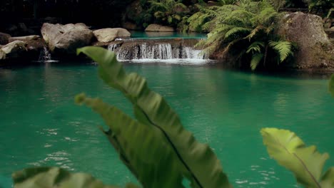 Ambient-motion-of-serene-tropical-waterfall-gently-cascading-and-flowing,-surrounded-by-lush-greenery-and-rocks