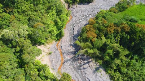 Aerial-drone-shot-descending-down-onto-a-remote-dry-riverbed-surrounded-by-forest-trees,-Risaralda,-Colombia