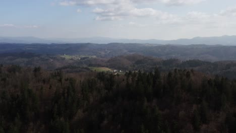 Misty-forested-landscape-stretching-into-soft,-hazy-mountains,-punctuated-by-pockets-of-open-fields-and-remote-homesteads