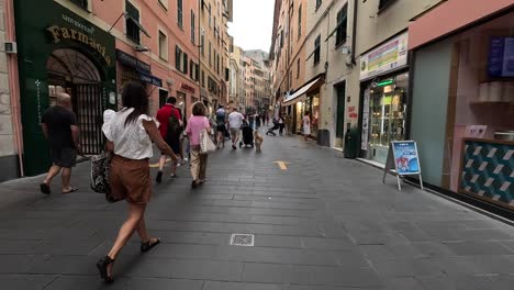 Handheld-point-of-view-clip-walking-down-busy-pedestrianised-street-with-shops-and-tall-buildings-on-both-sides