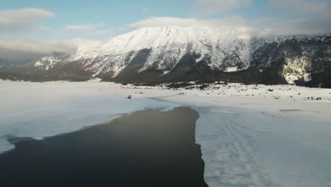Luftaufnahmen-Eines-Halb-Geschmolzenen-Sees-Mit-Einem-Schneebedeckten-Berg-Im-Hintergrund-Bei-Sonnenuntergang