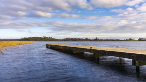 Time-lapse-of-a-concrete-lake-pier-in-the-foreground-and-castle-ruin-island-with-forest-in-distance-on-a-cloudy-sunny-day-at-Lough-Key-in-county-Roscommon-in-Ireland