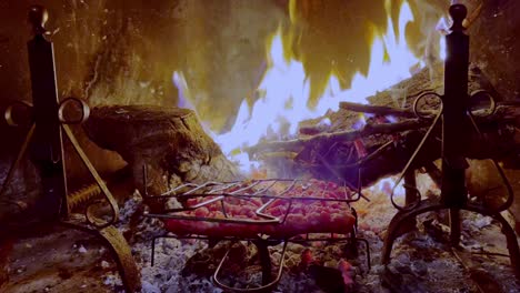 Delicious-sausages-roasting-on-fireplace-grill-with-fire-burning-in-background,-Close-up