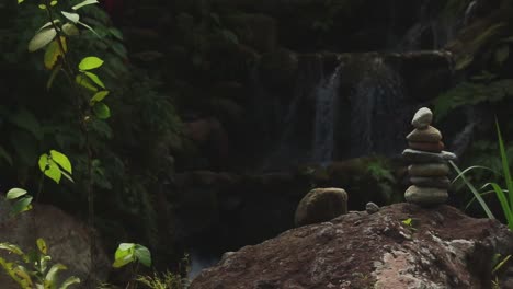 Eine-Ruhige-Szene-Mit-Einem-Steinstapel-Vor-Einem-Sanften-Wasserfall,-Umgeben-Von-üppigem-Grün