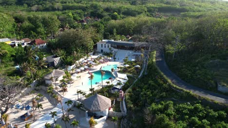 High-angle-aerial-shot-of-Cactus-Beach-Club-with-a-luxury-swimming-pool-and-green-trees-view-in-Nusa-Penida,-Bali,-Indonesia