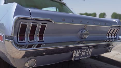 Slowmotion-close-up-panning-view-of-the-rear-end-of-a-blue-Ford-Mustang-on-a-sunny-day