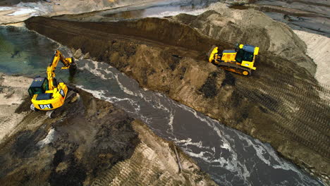 Aerial-overview-of-heavy-bulldozer-and-excavator-operating,-moving-dirt-in-the-diversion-of-pond-site