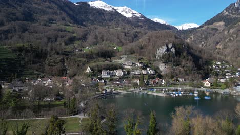 Clip-De-Drone-Alejándose-Del-Lago-Walen-Y-Del-Pueblo-De-Weesen,-En-La-Ladera-De-Una-Colina,-En-St-Gallen,-Con-Pintorescas-Montañas-Nevadas-Al-Fondo