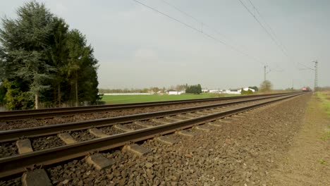 Red-Deutsche-Bahn-cargo-train-speeding-along-tracks,-daytime,-rural-landscape