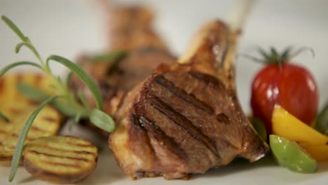 Chuletas-De-Cordero-A-La-Parrilla-Con-Romero,-Centrándose-En-La-Carne-Con-Verduras-Borrosas-En-El-Fondo,-Cocina-De-Alta-Gama