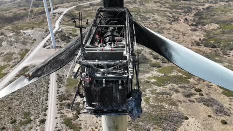 Vista-Aérea-De-Primer-Plano-De-Una-Turbina-Eólica-Destruida-Por-El-Incendio-En-Un-Paisaje-árido-Y-Montañoso-En-España