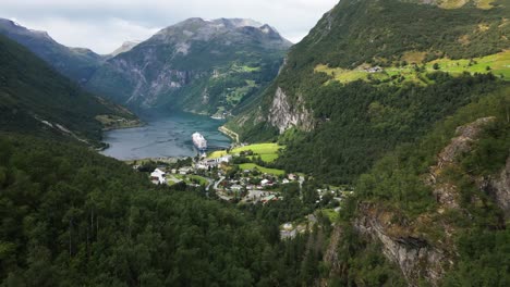 beautiful-green-valley-in-a-mountain-range-with-a-fjord-or-lake-and-a-cruise-ship-in-the-harbor,-norway,-europe,-drone