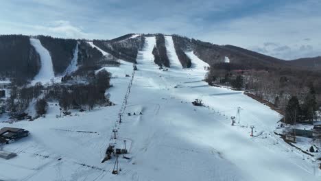 Disparo-Ascendente-De-Un-Dron-Volando-Muy-Por-Encima-De-La-Zona-De-Esquí,-Moviendo-Telesillas-Y-Esquiadores-Y-Practicantes-De-Snowboard-Debajo